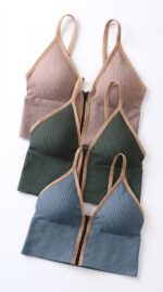 Tres bralettes acanalados con cremallera frontal en rosa empolvado, verde bosque y azul pizarra con ribete beige, en plano.
